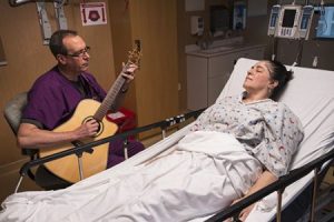 man with guitar playing for a person in a hospital bed