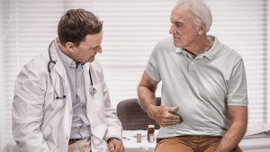 an older man touches his side while a doctor looks at the area