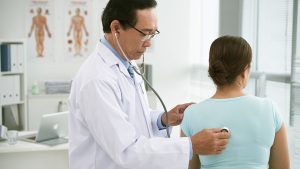 a doctor listens to a woman's back with his stethoscope in a medical office