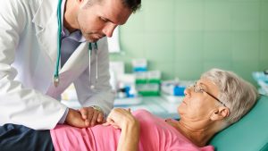 a woman lays on an exam table while the doctor leans over her and presses on her stomach