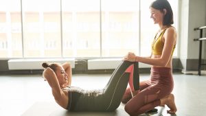 a woman in a gray exercise outfit does setups while another woman helps hold her knees